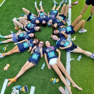 Group pic of a team laying in the grass with their heads together in a circle